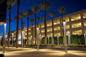 Illuminated multi-story parking structure at dusk, flanked by tall palm trees and modern light poles along a landscaped walkway